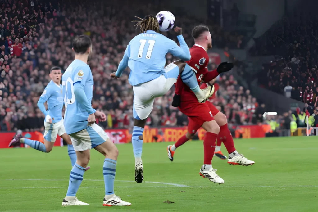 Jeremy Doku kicking the ball towards McAlister while Bernardo Silva and Phil Foden look on during the match between Liverpool and Manchester City at Anfield.